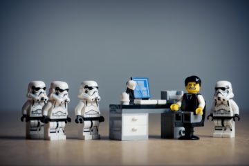 Lego Stormtroopers surrounding an uncomfortable Lego man at his desk