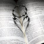 Crown of thorns on an open Bible, casting a shadow in the shape of a heart