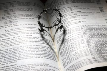 Crown of thorns on an open Bible, casting a shadow in the shape of a heart